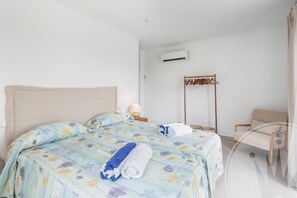 Ein Hotelzimmer mit einem großen Bett, einem Holzbstuhl, einem Garderobenhaken und einer Klimaanlage an der Wand.