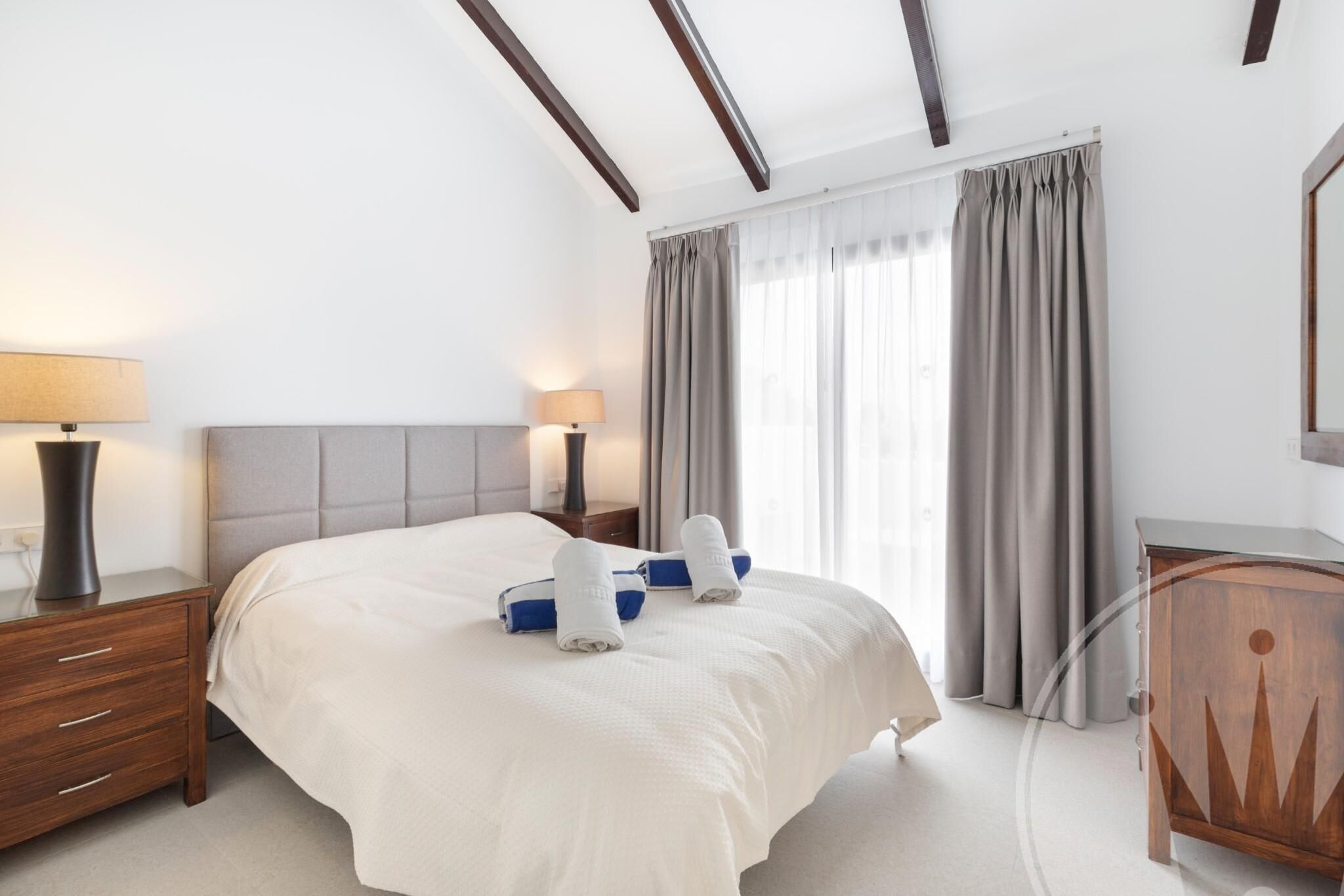Habitación de hotel con cama, mesitas de noche, lámpara, armario y ventana con cortinas.