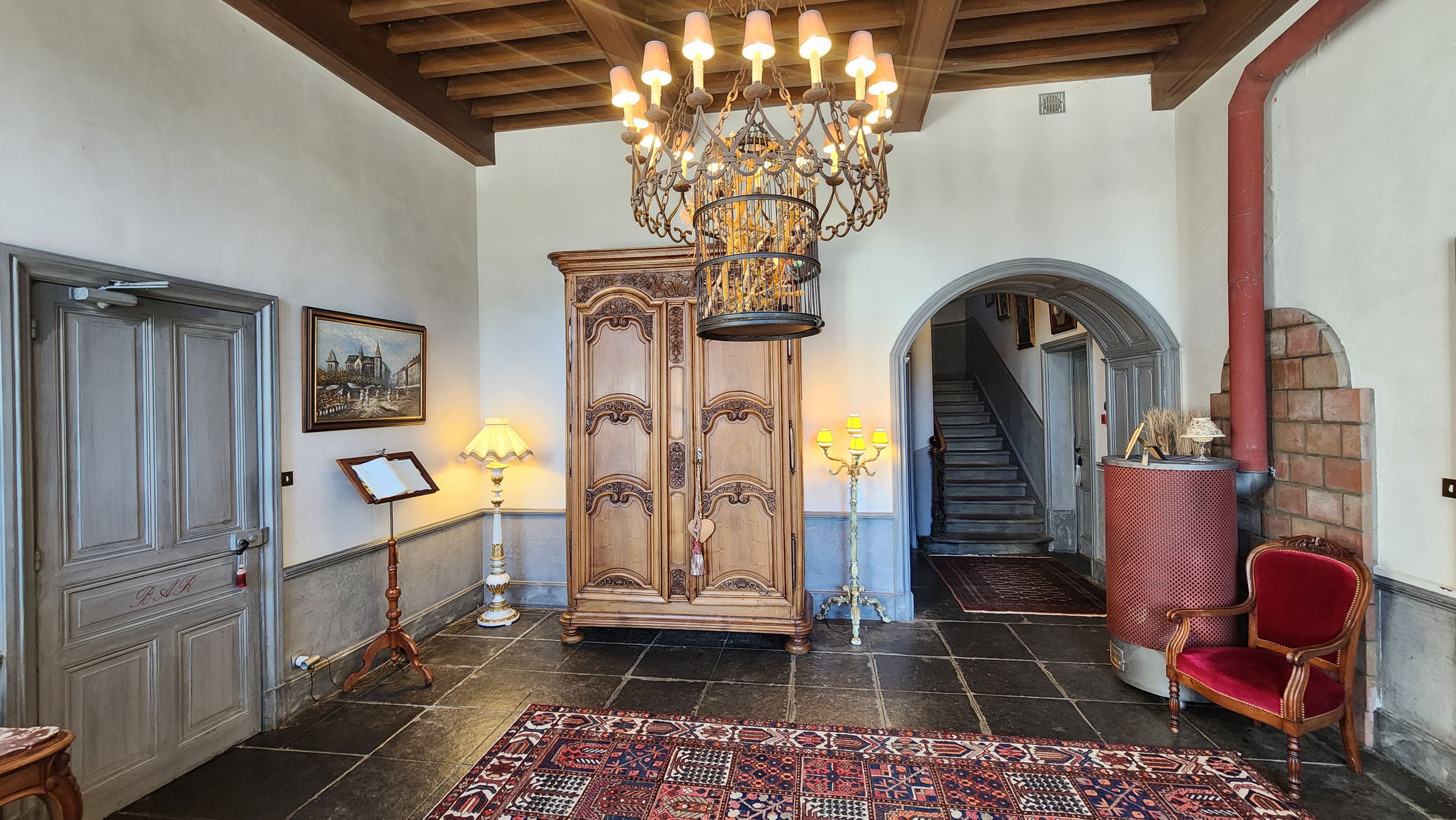 Un hall majestuoso con un candelabro, una silla roja y una escalera que lleva a otra habitación.