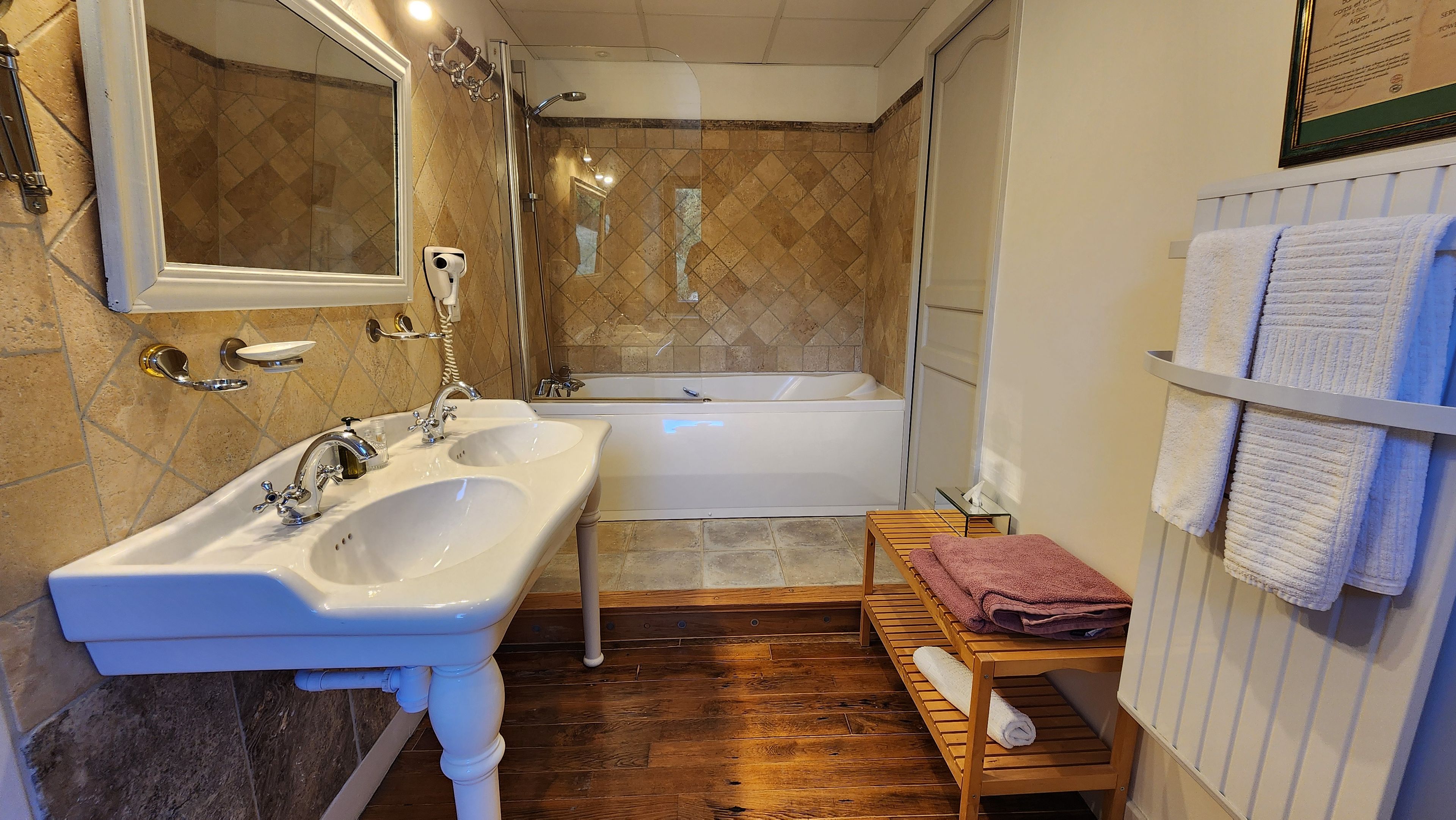 A bathroom with a double sink, a bathtub, and a wooden bench.