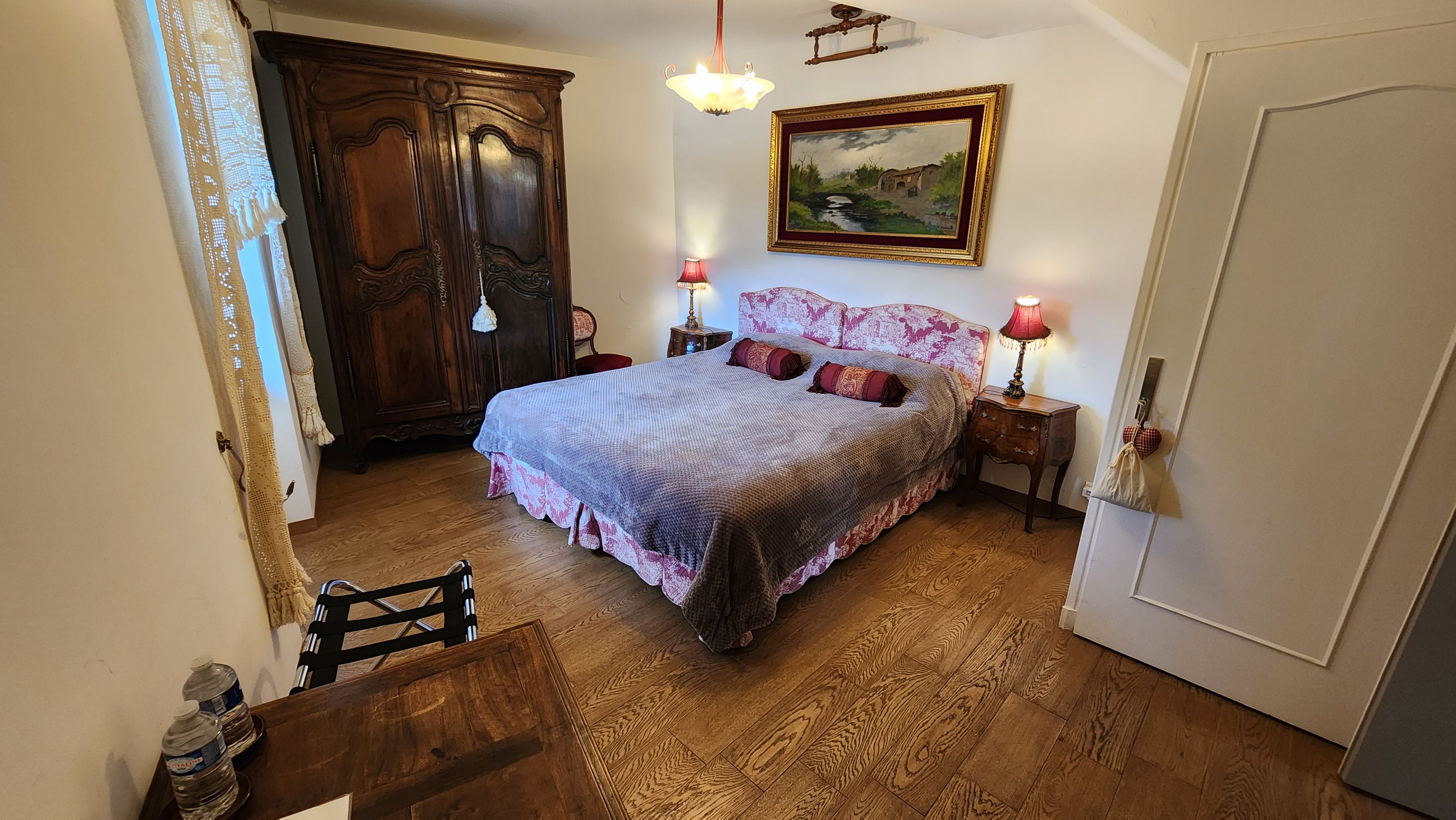 A bedroom with a large bed, wooden wardrobe, and a painting on the wall.