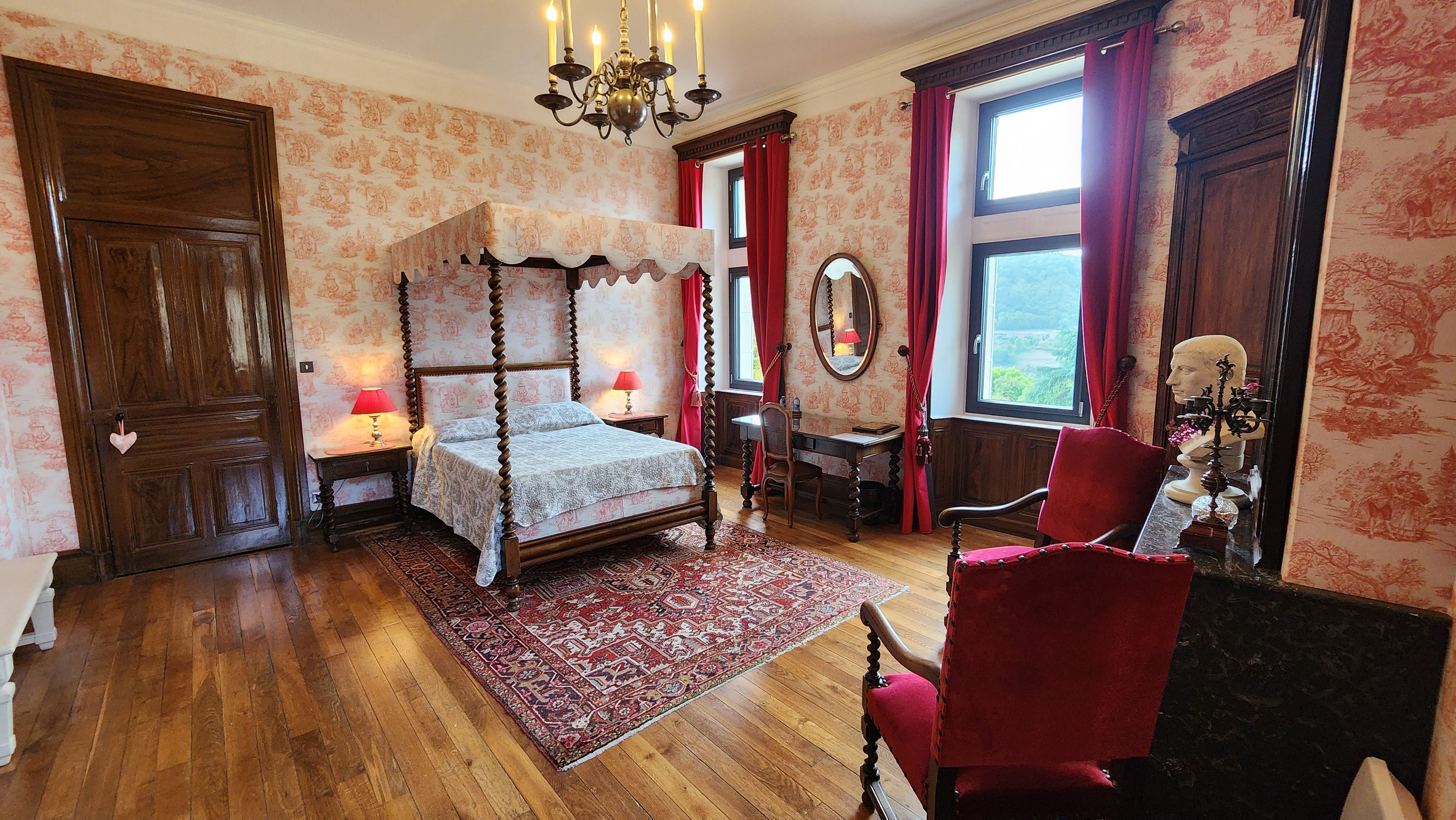 Een klassieke slaapkamer met een hemelbed, bureau, stoel en grote spiegel.
