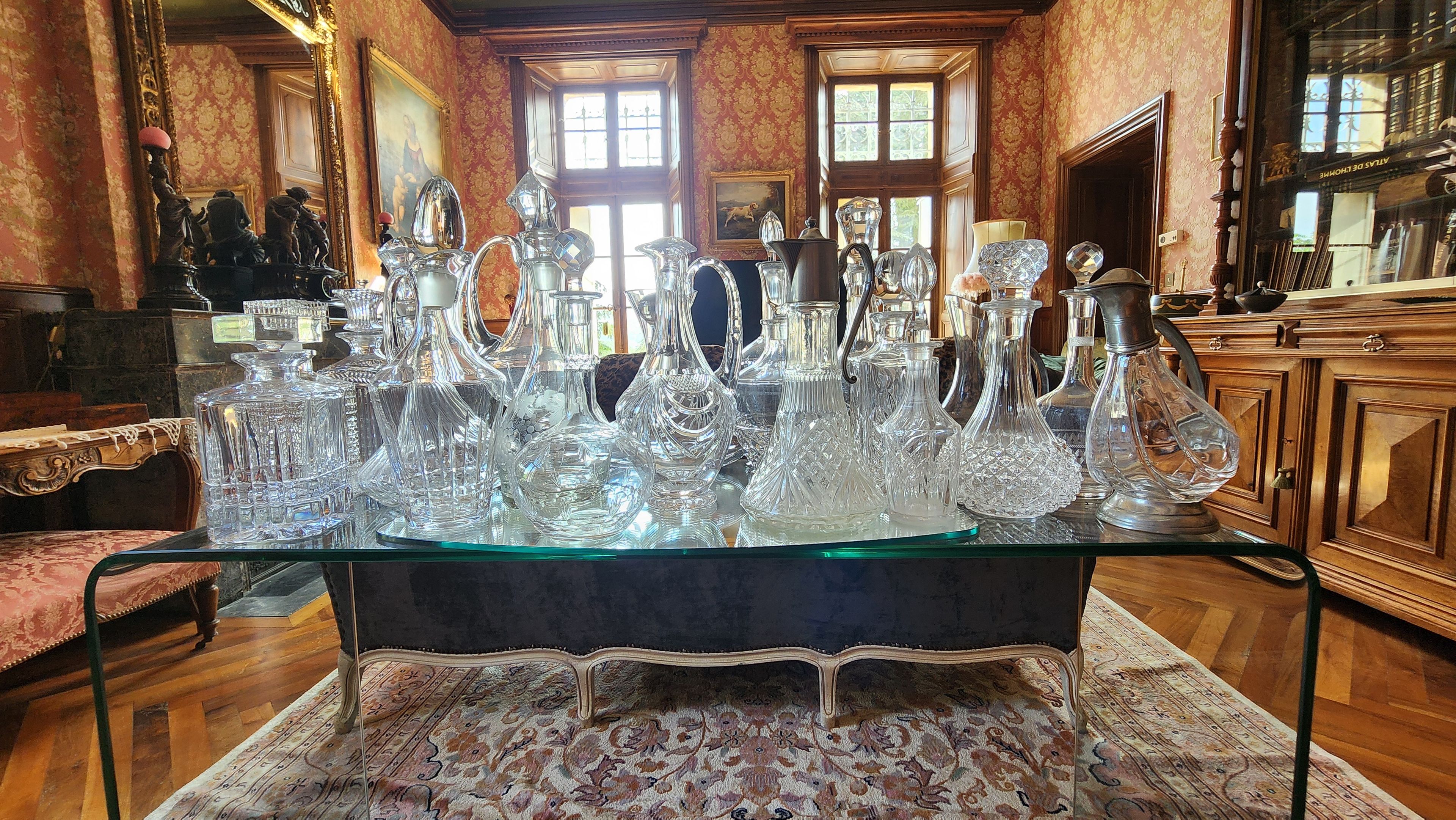 A room with a glass display table featuring various crystal decanters and pitchers.