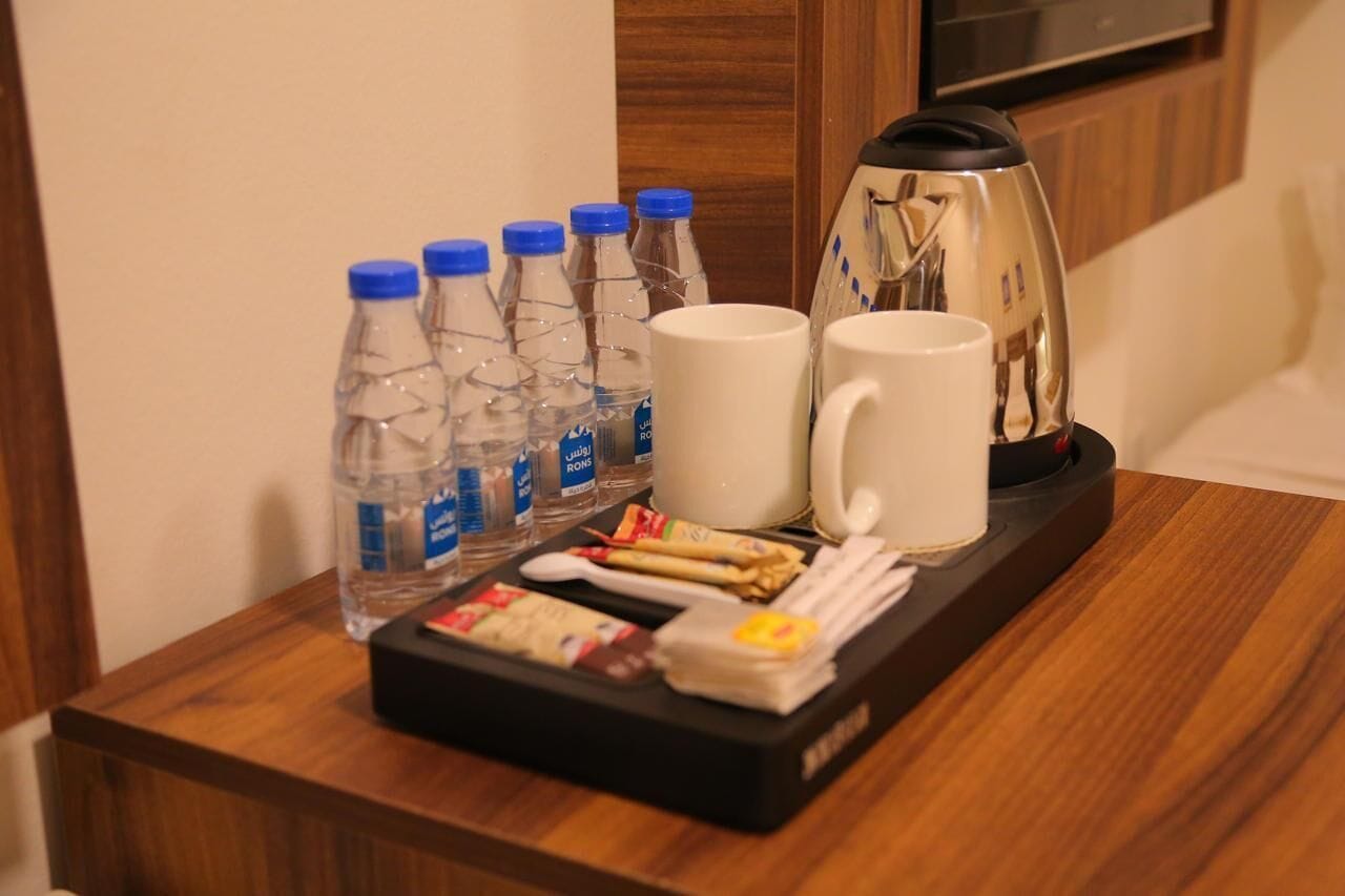 A tray with bottled water, a coffee pot, two white mugs, a box of tissues, and a small container of cream.