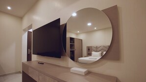 A modern bathroom with a large mirror, a flat-screen TV, and a vanity with a towel bar. - Jada  Apartments (AL KHOBAR)