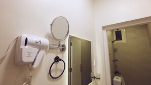 A hair dryer mounted on a wall with a mirror above it, a towel ring, and a shower area visible through an open door. - Jada  Apartments (AL KHOBAR)