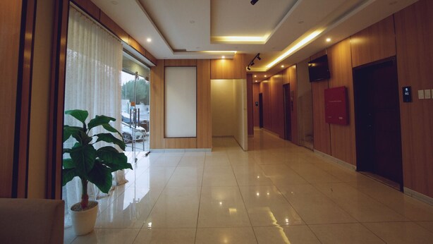 A hotel hallway with a potted plant, a door with a red sign, and a wall-mounted television. - Jada  Apartments (AL KHOBAR)
