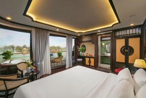 A hotel room with a large bed, a balcony with a view of the water, a small table with a plant, and a bathroom with a mirror and sink. - Hermes Premium Cruise (Hong Gai)