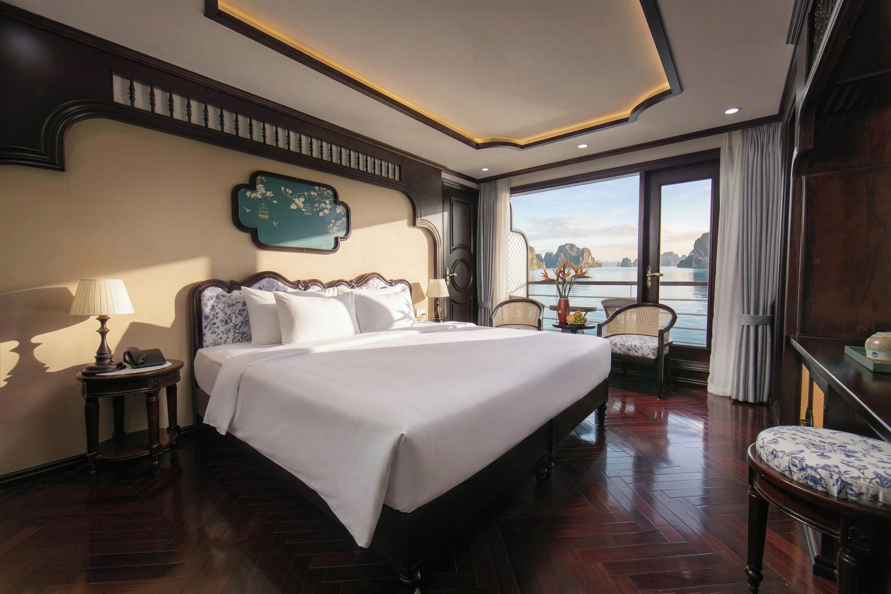 Een hotelkamer met een groot bed, uitzicht op zee en een balkon met een tafel en stoelen.