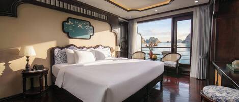 Een hotelkamer met een groot bed, uitzicht op zee en een balkon met een tafel en stoelen.