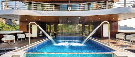 Un espace piscine à plusieurs niveaux, comprenant un jacuzzi, des chaises longues et une vue sur le paysage environnant.
