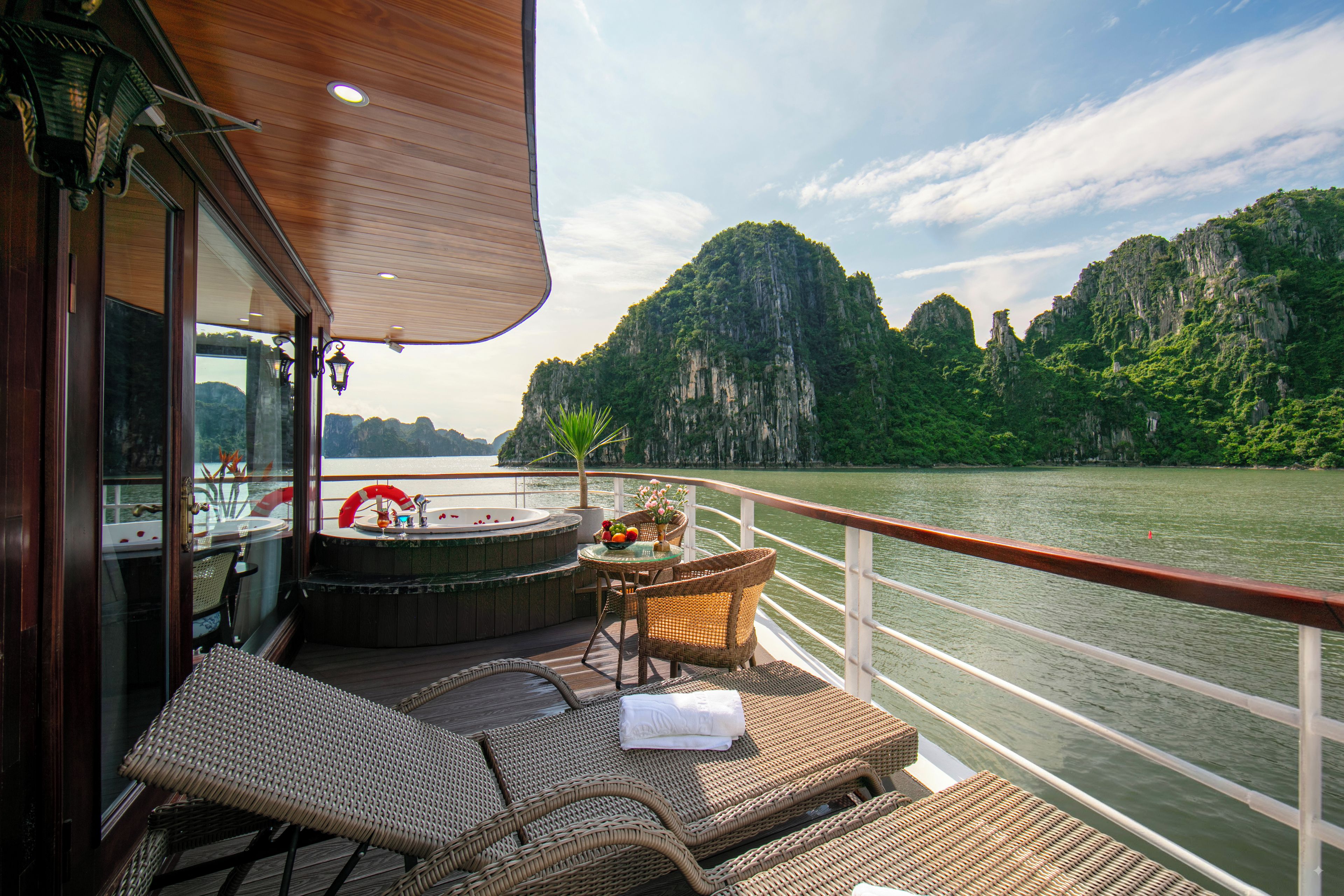 A deck with wicker furniture, a hot tub, and a view of a river and mountains.