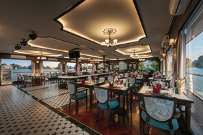 A restaurant with multiple dining tables and chairs, a patterned floor, and a view of the water outside. - Hermes Premium Cruise Ha Long Bay (Hon Gai)