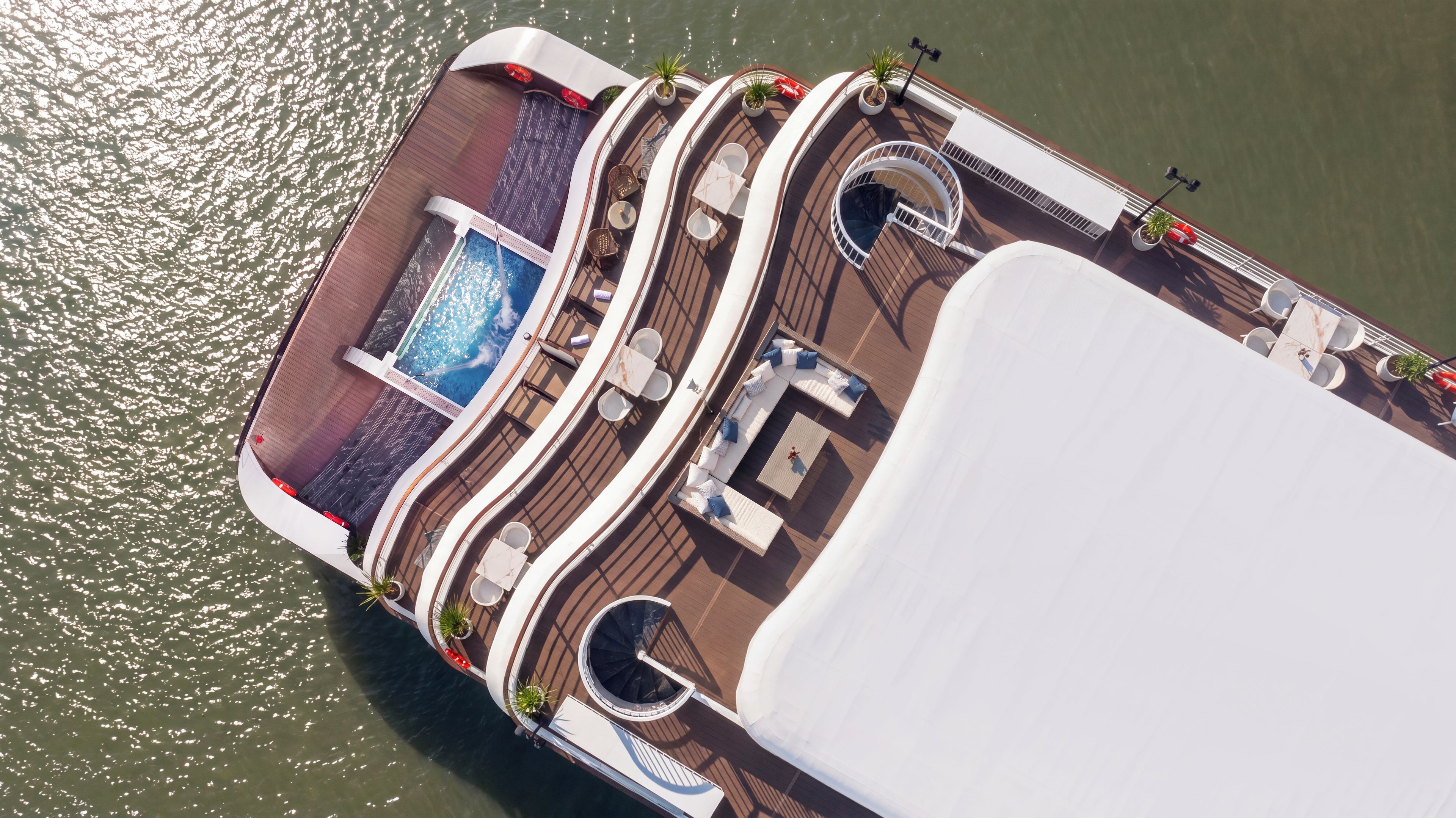 An aerial view of a cruise ship's deck with a swimming pool, sun loungers, and a covered dining area.