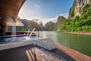 A hot tub on a wooden deck with a view of a river and mountains. - Hermes Premium Cruise (Hong Gai)