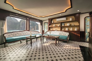 A room with a large window, two sofas, a coffee table, and a wall with shelves. - Hermes Premium Cruise Ha Long Bay (Tuan Chau)