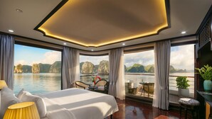 Quarto espaçoso com uma cama grande, área de estar com mesa e vista para um corpo de água com montanhas.