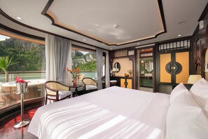 A hotel room with a large bed, a desk with a chair, a view of the outdoors, and a bathroom with a mirror and sink. - Hermes Premium Cruise (Hong Gai)