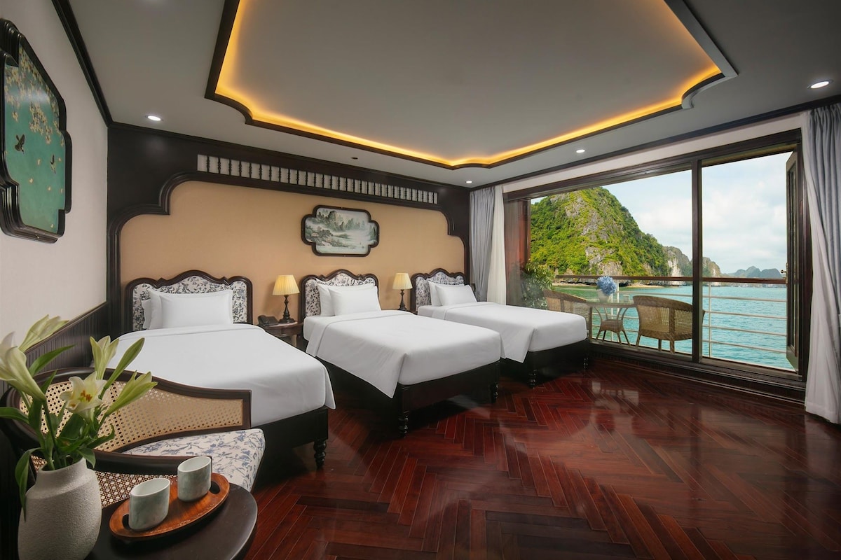 Quarto de hotel com duas camas, uma janela grande com vista para o mar e teto com iluminação embutida.