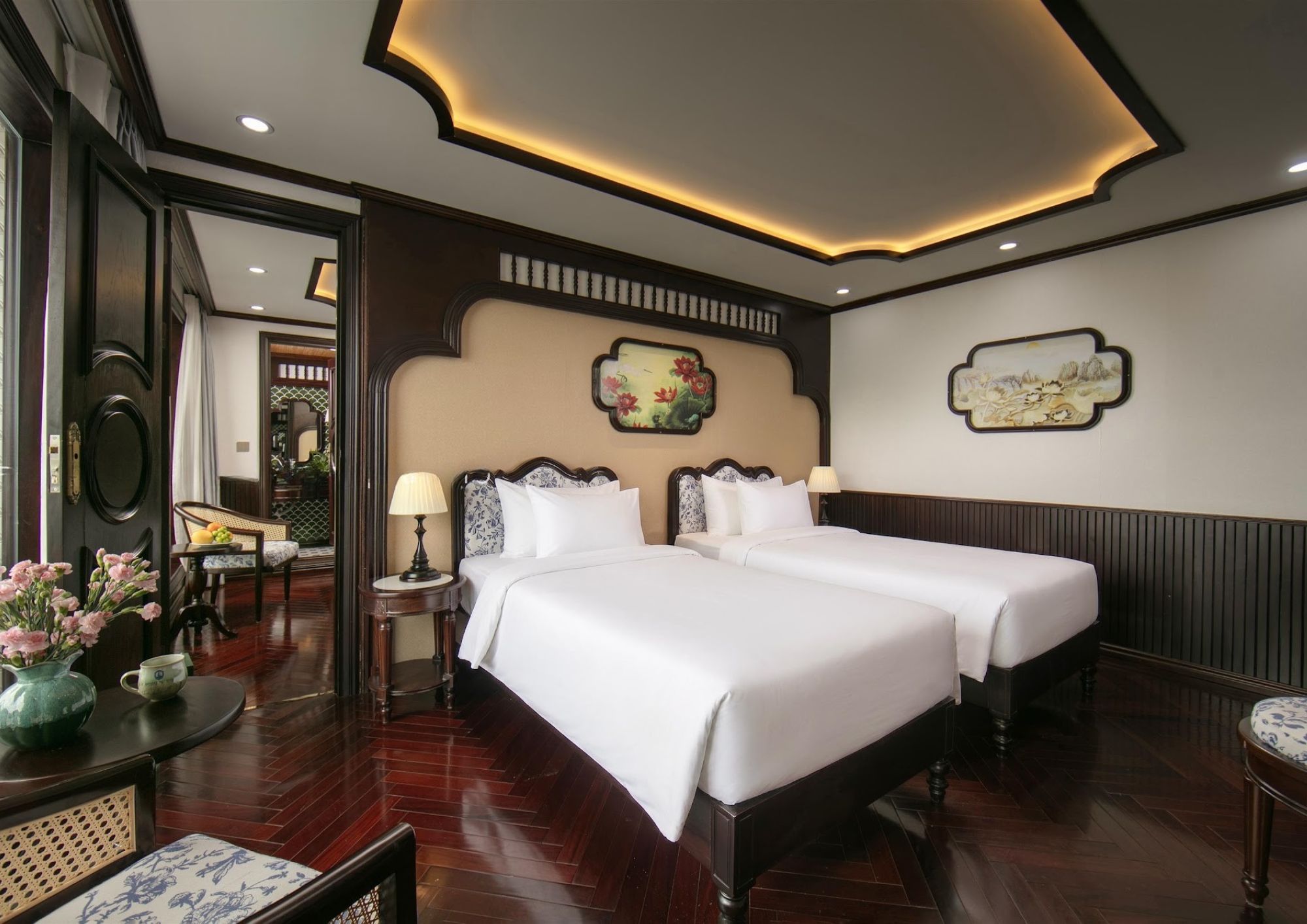 A hotel room with two beds, a sitting area with a chair and table, and artwork on the walls.