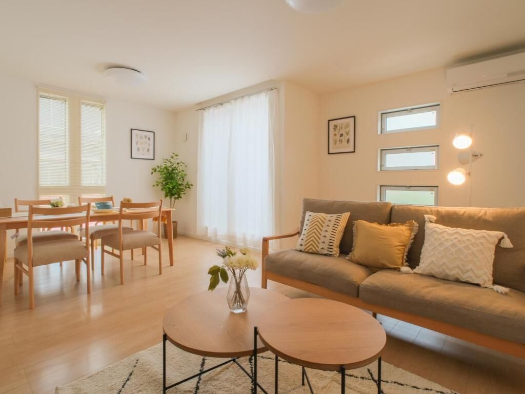 A living room with a sofa, coffee table, dining table, chairs, and a plant.