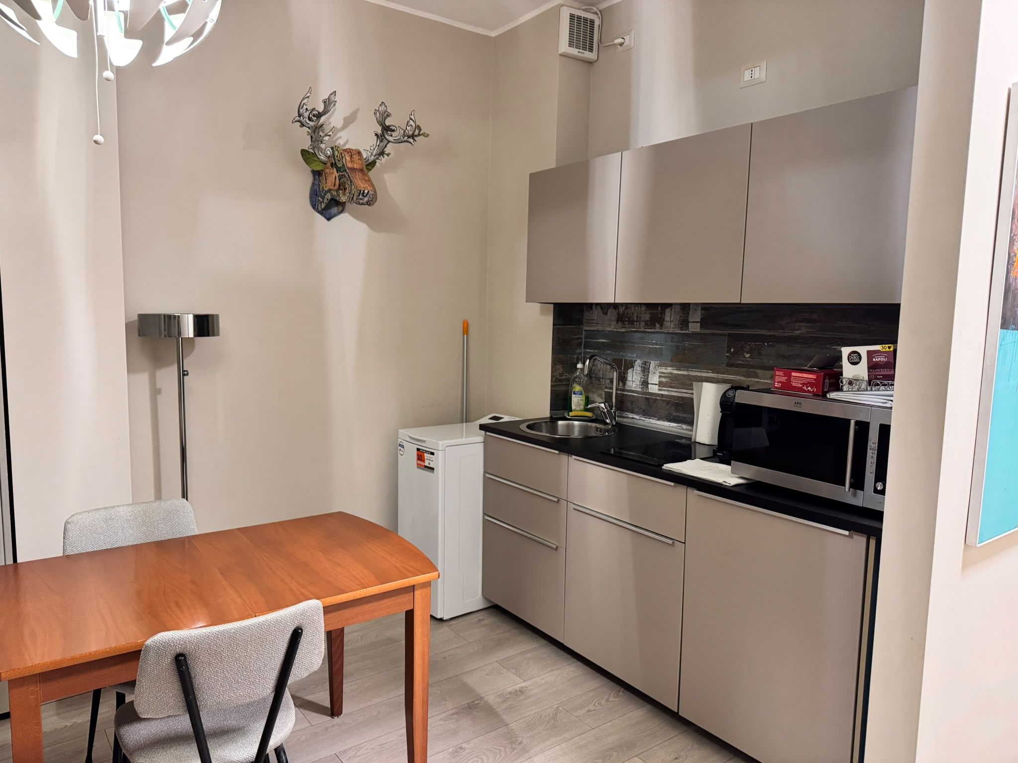 A compact kitchen with a wooden dining table, a white refrigerator, and stainless steel appliances.
