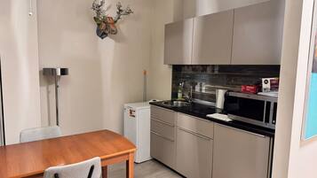 A compact kitchen with a wooden dining table, a white refrigerator, and stainless steel appliances.