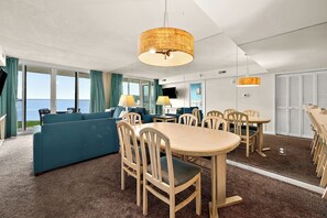 Ein Hotelzimmer mit großem Fenster, einer Couch, einem Esstisch mit Stühlen und einem Fernseher.
