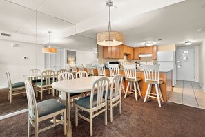 A modern kitchen with wooden cabinets, a central island, and a dining area with chairs and a table. - Bayfront Retreat Near Jolly Roger | Indoor Pool & Private Patio (Ocean City)