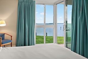 A room with a bed, a chair, and a view of a body of water through a glass door. - Bayfront Retreat Near Jolly Roger | Indoor Pool & Private Patio (Ocean City)