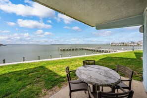Eine Terrasse im Freien mit Tisch und Stühlen, mit Blick auf ein Gewässer und einen Steg, der sich ins Wasser erstreckt.