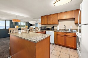 A modern kitchen with granite countertops, wooden cabinets, a built-in dishwasher, and a large island with seating. - Bayfront Retreat Near Jolly Roger | Indoor Pool & Private Patio (Ocean City)