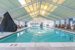 Ein überdachter Innenpool mit Panoramafenstern und Liegestühlen um den Pool.