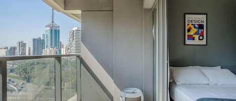 A modern hotel room with a balcony, a bed, a wall-mounted artwork, and a city view.