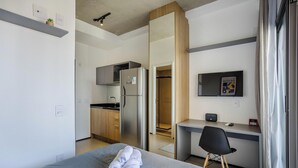 A compact hotel room with a kitchenette, a bed with a rolled-up towel, a desk, and a chair. - Studio in Cond. w/ Pool in Paraiso Onp1701 (São Paulo)