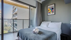 A hotel room with a large window, a bed with white linens, and a framed Bauhaus Design poster on the wall. - Studio in Cond. w/ Pool in Paraiso Onp1701 (São Paulo)