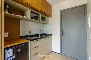 A compact kitchen with wooden cabinets, a built-in microwave, and a small refrigerator. - Studio w/ Balcony 10m From Subway Onp0913 (São Paulo)
