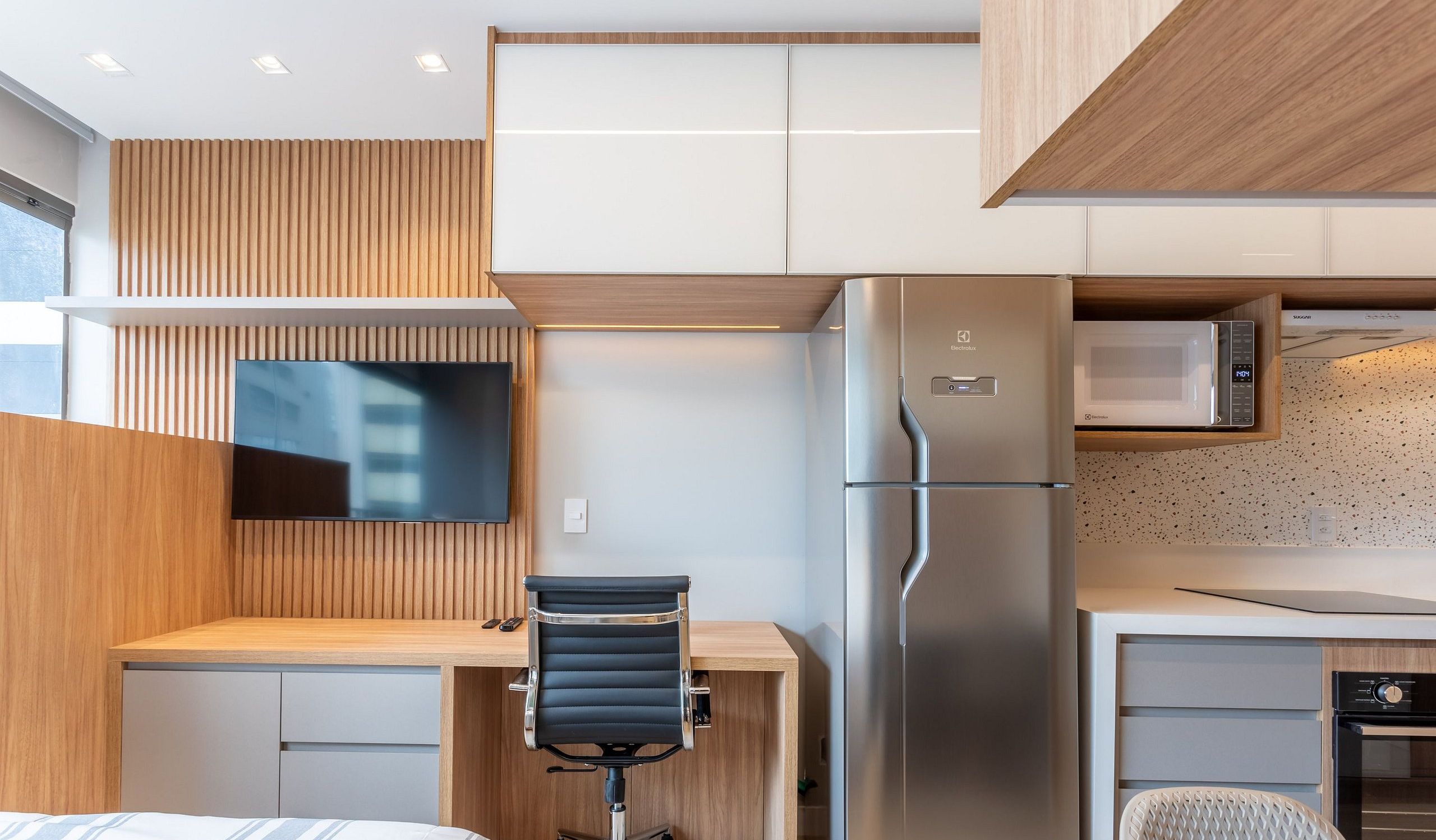 A modern kitchenette with a built-in microwave, refrigerator, and a flat-screen TV mounted on the wall.
