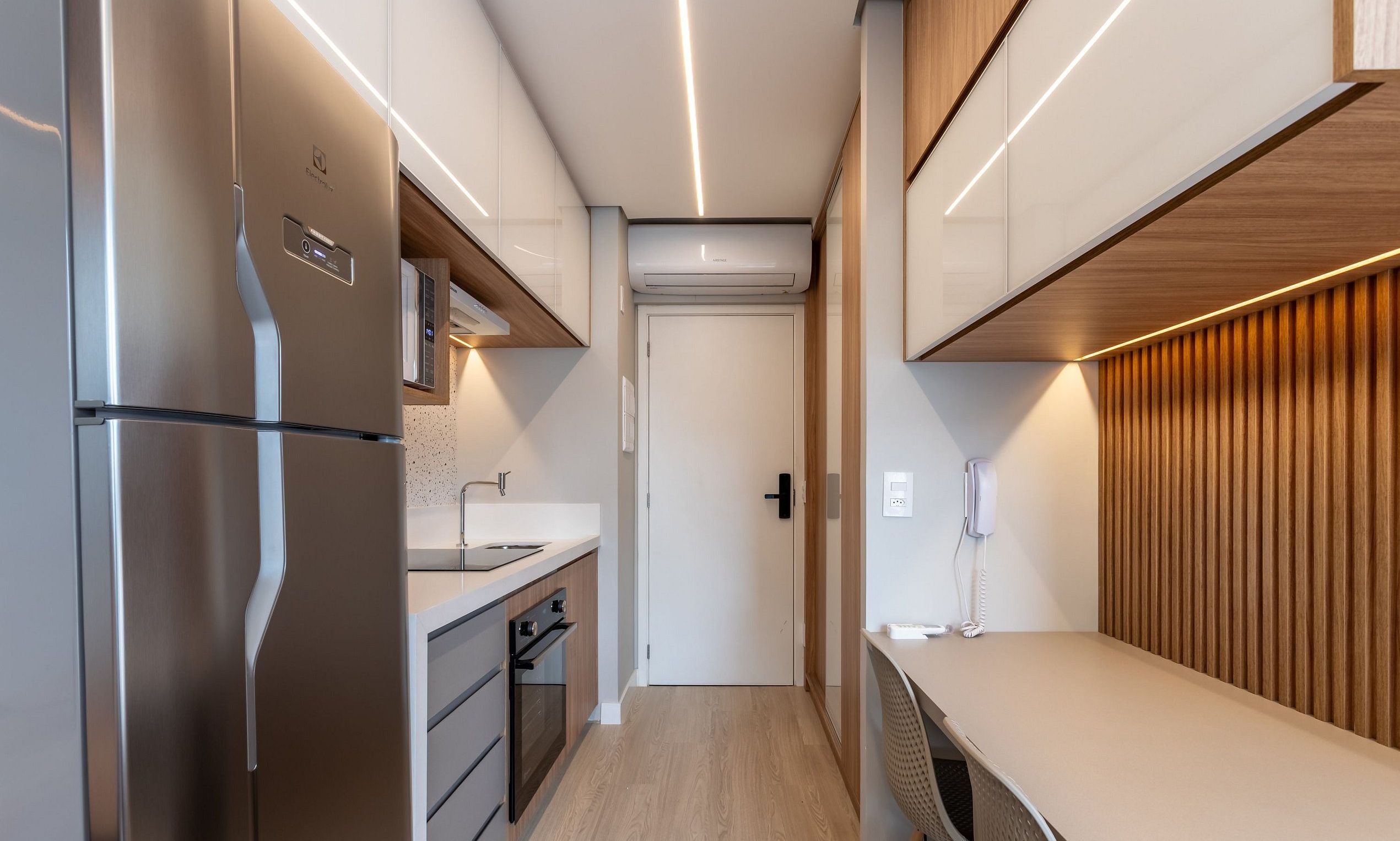 A compact kitchen with a refrigerator, oven, and a built-in air conditioning unit.