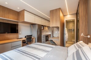 A modern bedroom with a large bed, a desk, and a kitchenette. - Modern Studio in Jardins - SP Oag0820 (São Paulo)
