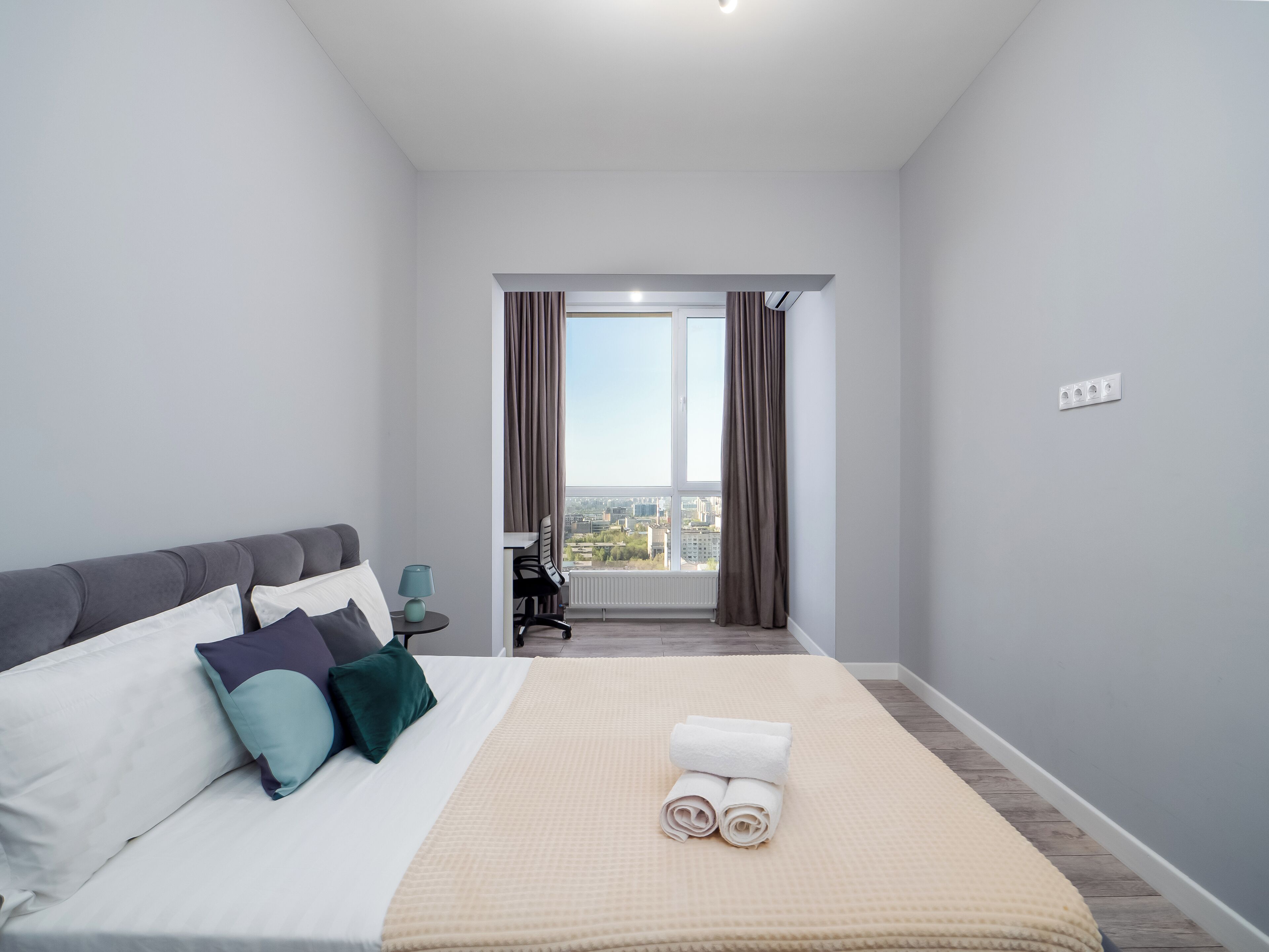A hotel room with a bed, a desk, a chair, and a view of the city.