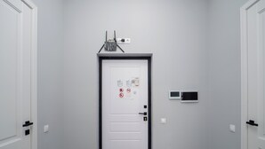 En gang med en hvid dør, et sort dørhåndtag, et intercom på væggen og en lille elektronisk enhed.