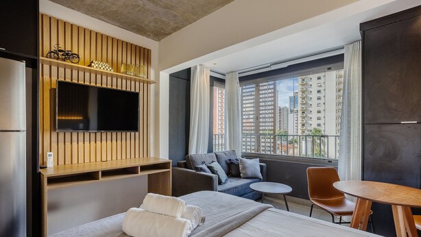 Una camera d'albergo moderna con un letto grande, un divano, un tavolino, una TV montata su un pannello di legno e un balcone con vista sulla città.