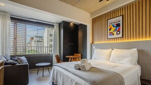 Camera d'albergo moderna con un letto grande, un tavolino rotondo, un divano e vista sulla città attraverso ampie finestre.