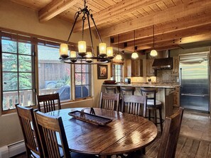 A wooden dining table with chairs, a chandelier, and a kitchen area with a refrigerator. - New to VRBO! Ski-in/out in 15 Steps - Alpine Meadows Chalet - Hot Tub -Mtn Views (Big Sky)