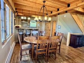 A wooden interior with a round dining table surrounded by chairs, a kitchen area with a refrigerator, and a staircase. - New to VRBO! Ski-in/out in 15 Steps - Alpine Meadows Chalet - Hot Tub -Mtn Views (Big Sky)