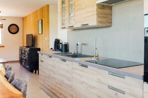 A modern kitchen with wooden cabinetry, a built-in stove, and a large island with a sink. - Le Grand Duc: Lake view and close to downtown (Gérardmer)