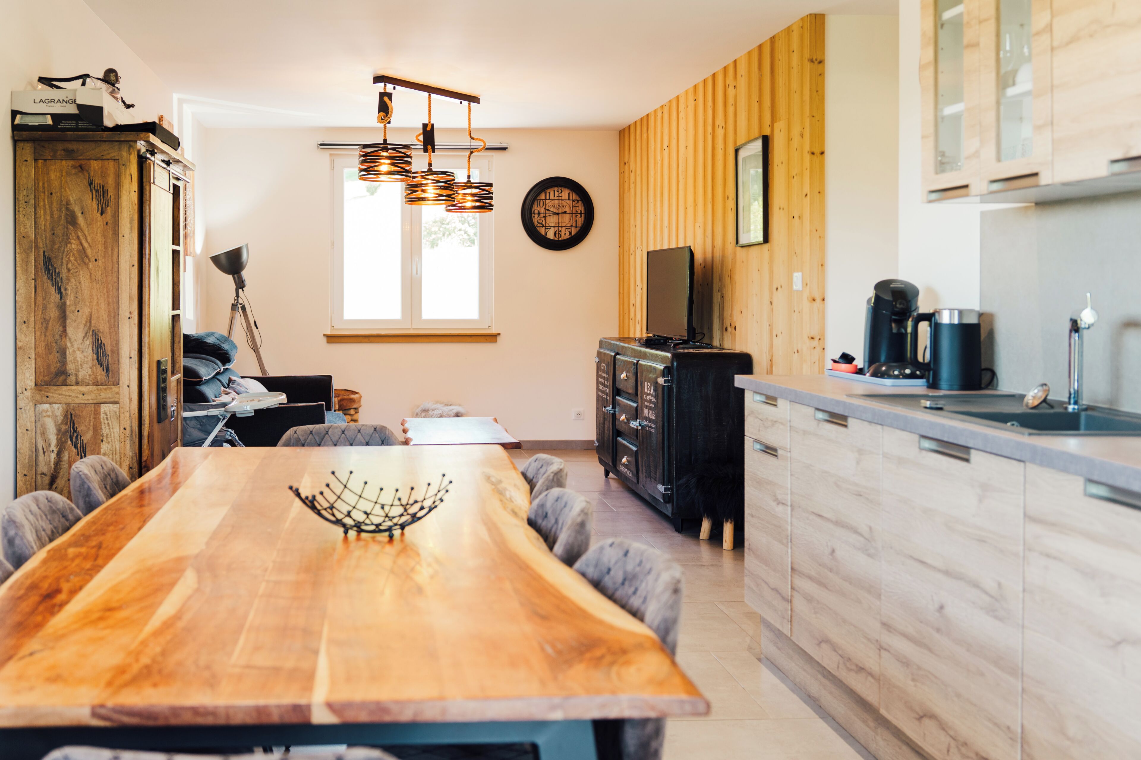 A modern kitchen with a wooden dining table, a built-in oven, and a coffee machine.