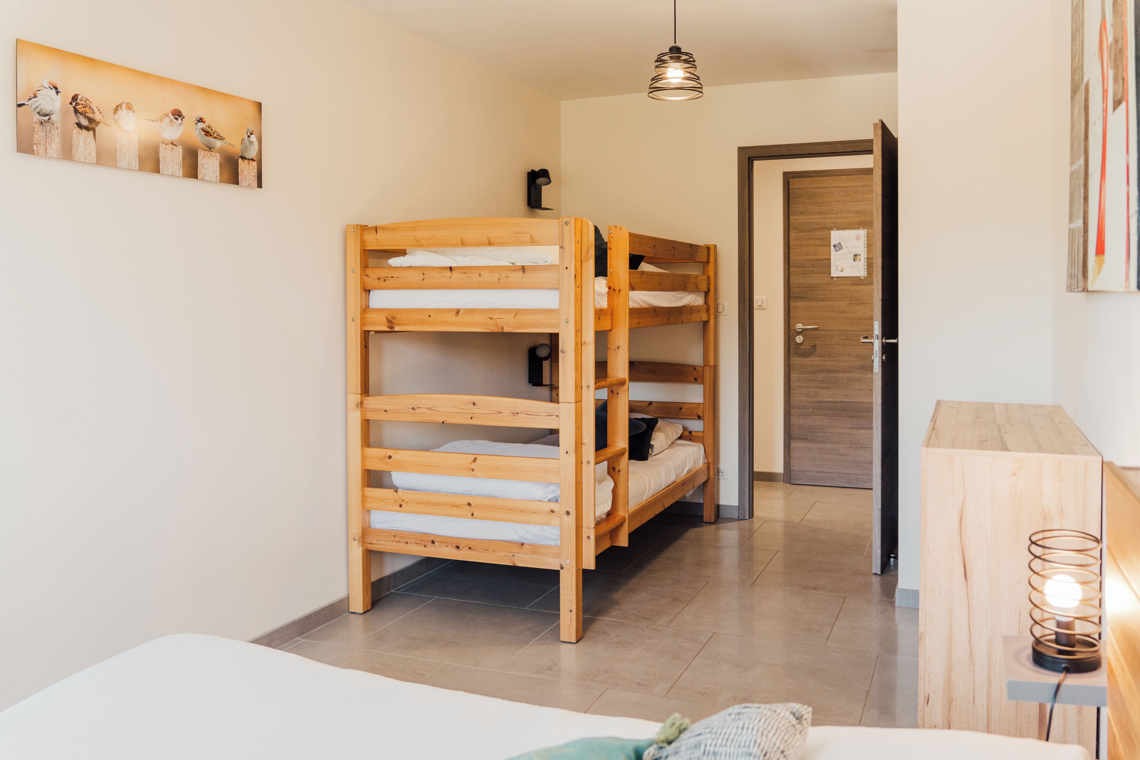 Une chambre avec un lit superposé, une tête de lit en bois, une table de chevet avec une lampe et un tableau accroché au mur.