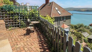 A house with a brick patio, a wooden fence, and a view of a lake. - Seaside Steps (Goodwick)